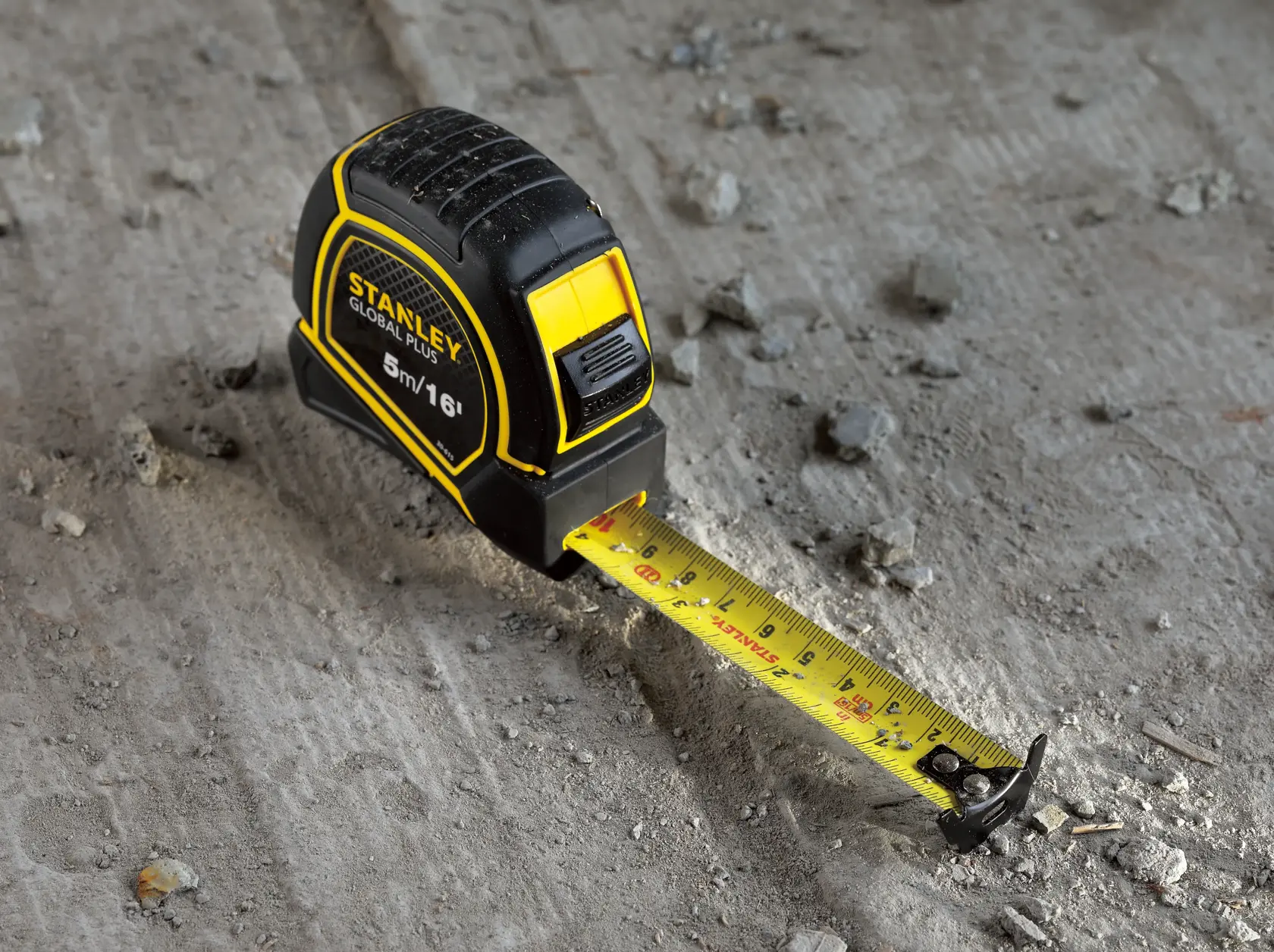 Cinta métrica STANLEY 30-615 con hoja amarilla y carcasa negra y amarilla, extendida sobre una superficie de concreto rugoso.