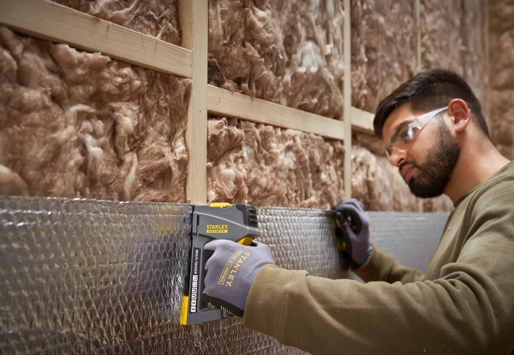 STANLEY FMHT6-70868 pistola de grapas utilizada sobre aislamiento por trabajador con guantes, obra en construcción.