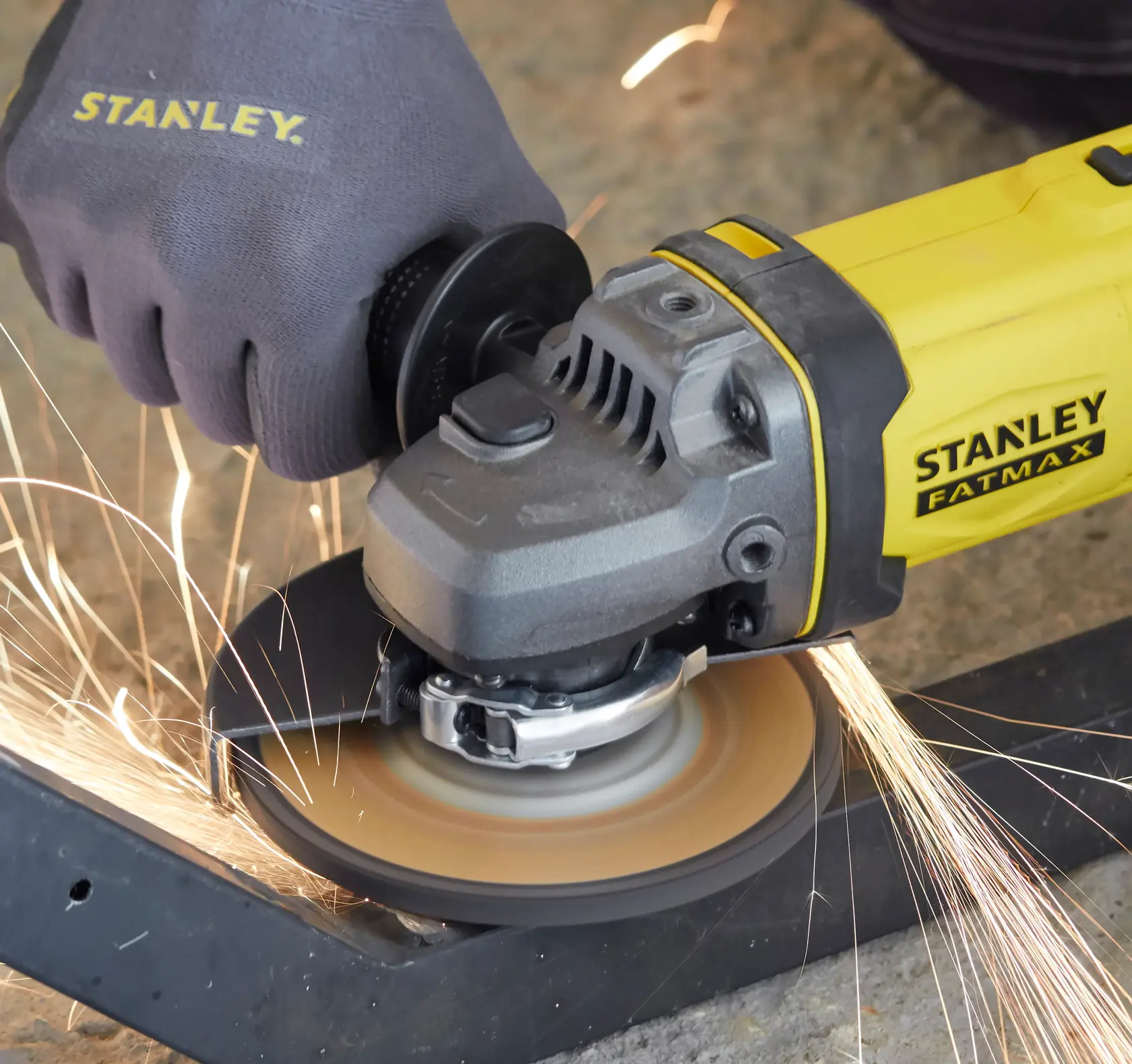 Amoladora angular STANLEY SCG400M2K-KR en uso, emitiendo chispas al cortar metal, vista cercana lateral.