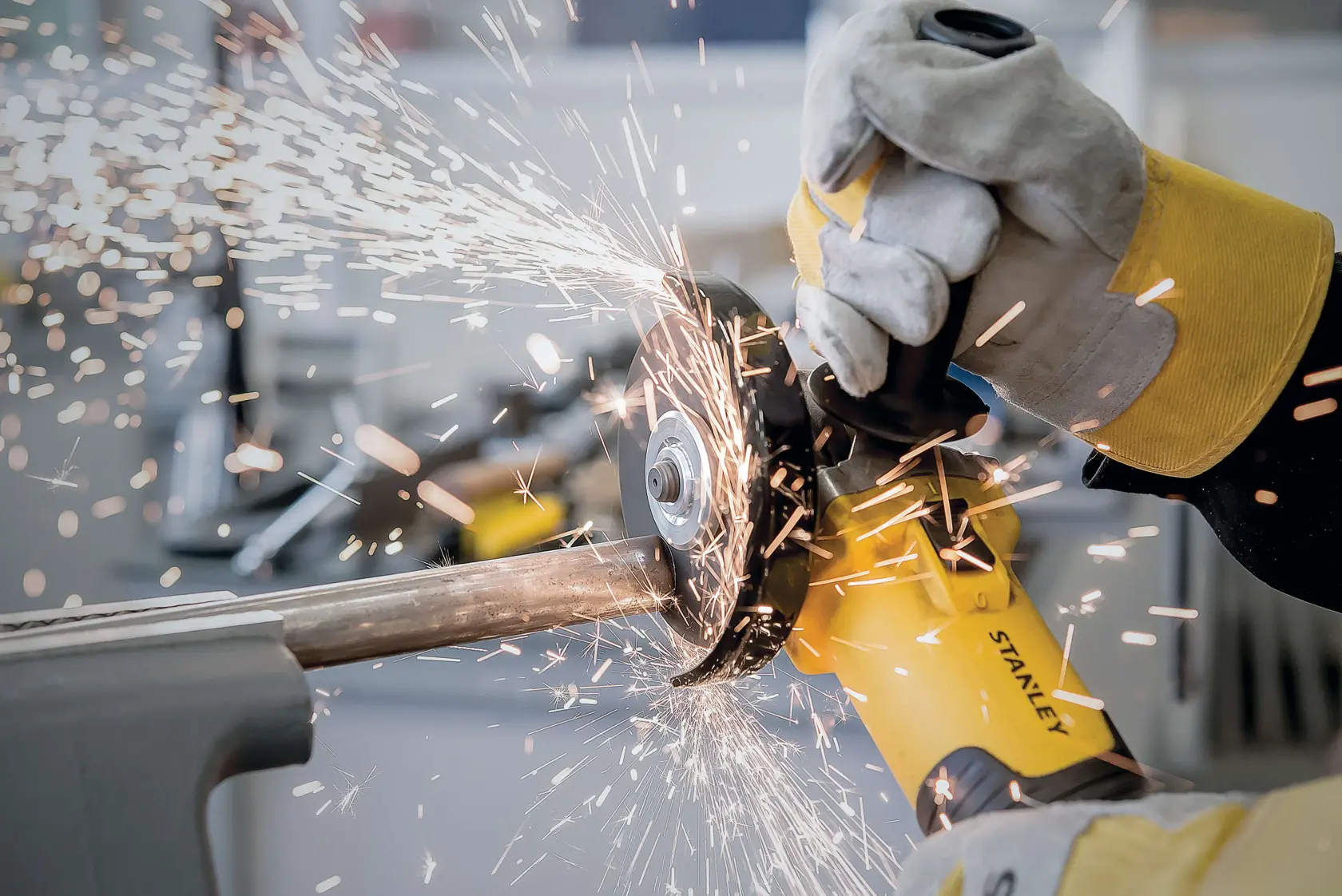 Fotografía de la amoladora angular STANLEY STA8061 en uso, con chispas al cortar un tubo de metal, toma de cerca.