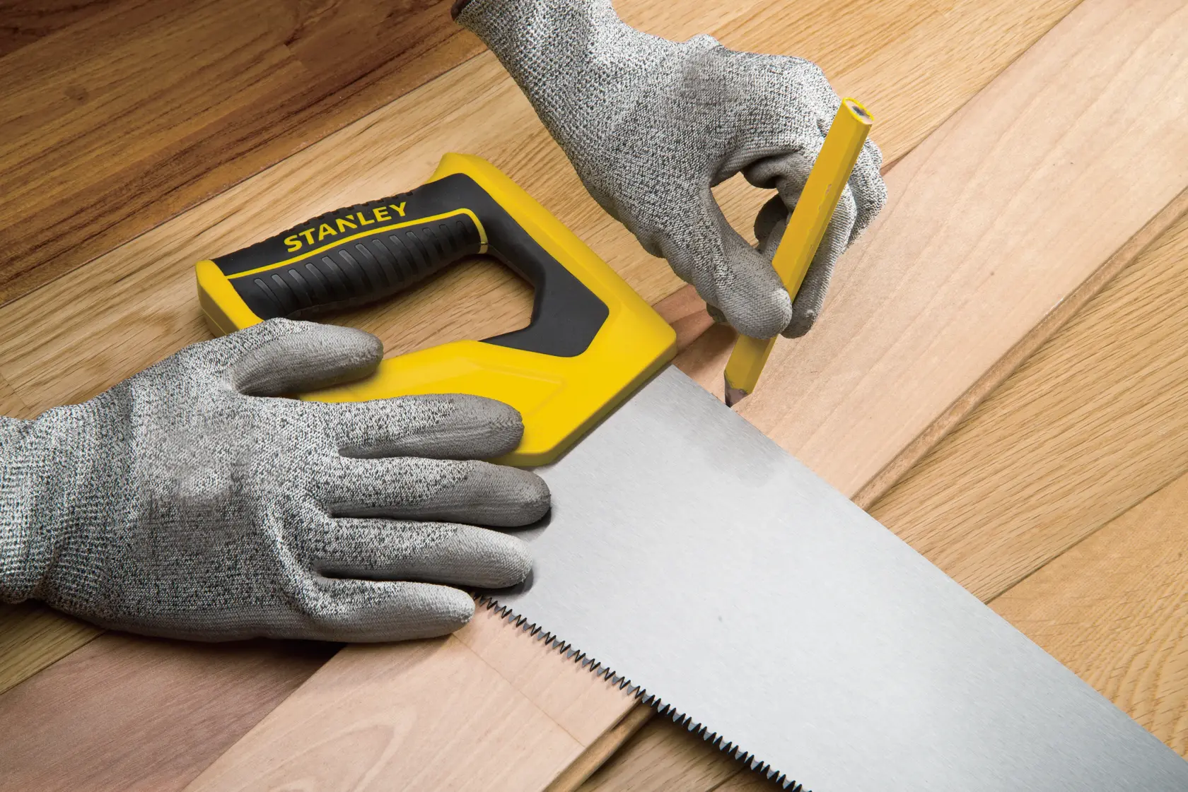 Fotografía de serrucho STANLEY STHT20375-LA con mango amarillo y negro sobre tablones de madera, manos con guantes marcando línea de corte.