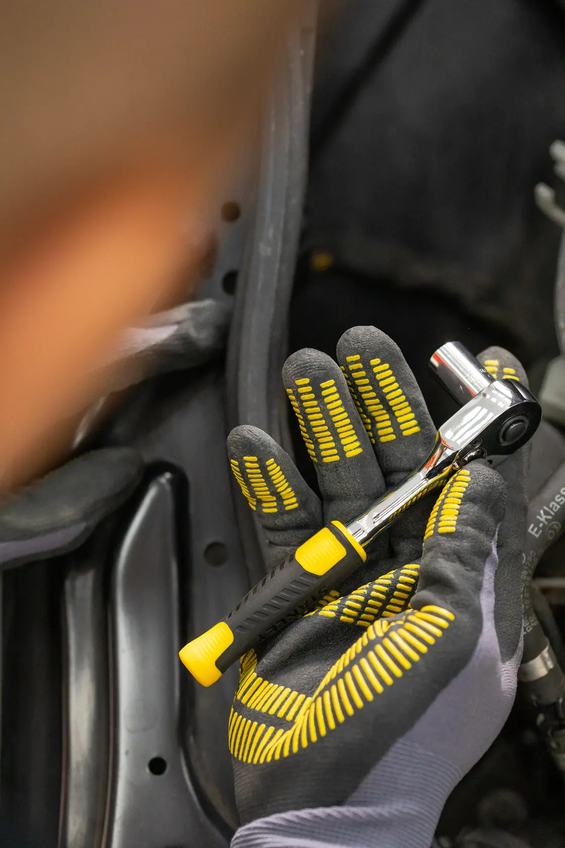 Fotografía de la llave de carraca STANLEY STMT82829-1 sostenida con guante, con mango negro y amarillo.