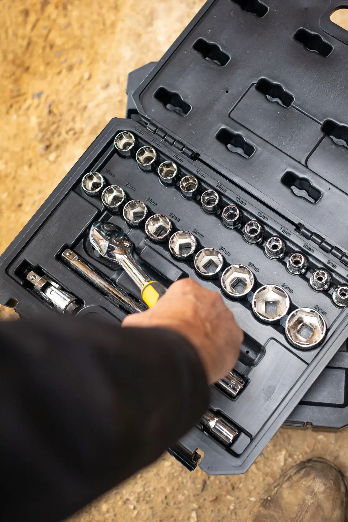 STANLEY STMT82830-1 juego de dados con carraca, dados y accesorios en estuche negro, mano acercándose a la herramienta.