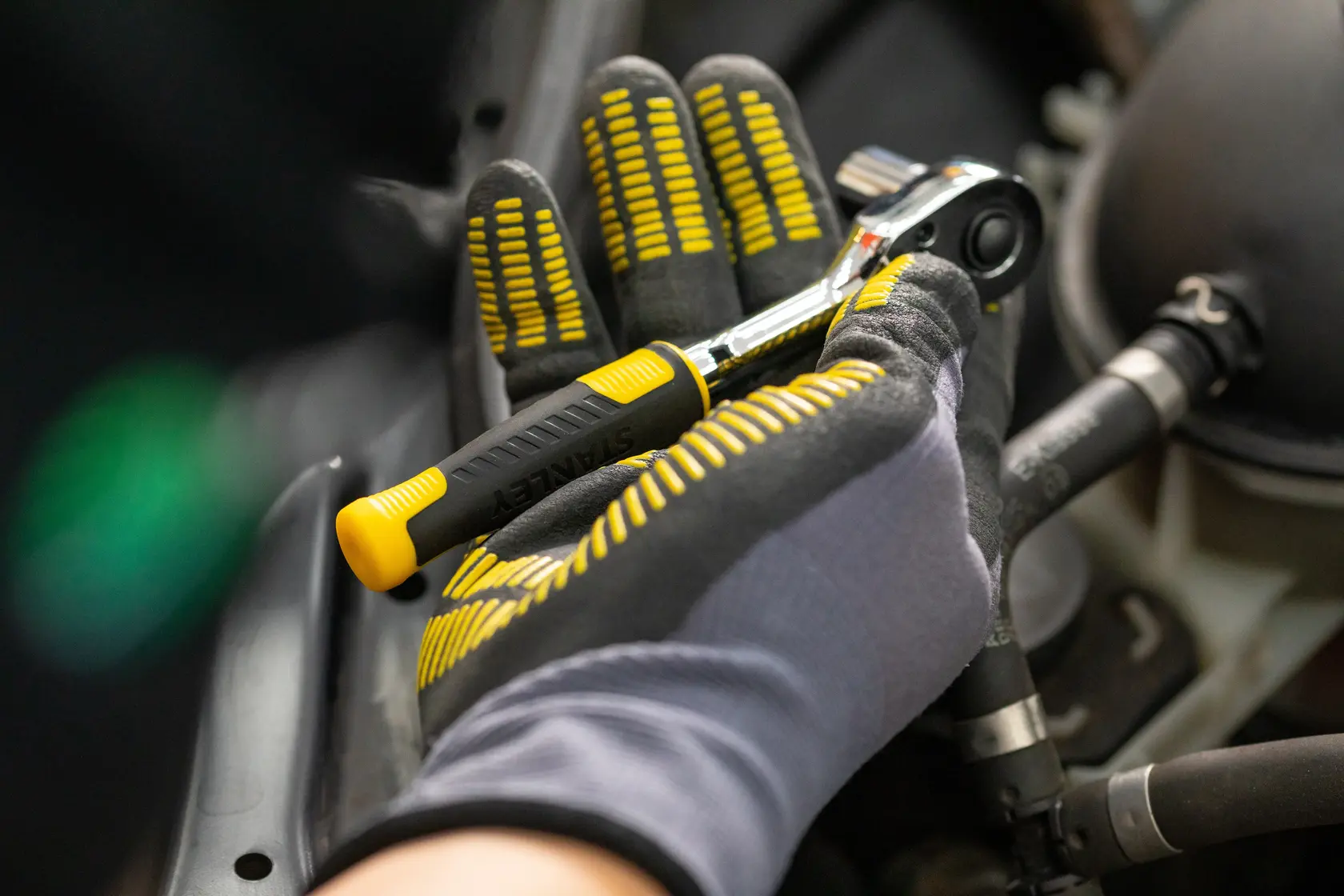 STANLEY STMT82832-1 carraca con empuñadura negra y amarilla sostenida por mano enguantada, detalle en trabajo automotriz.