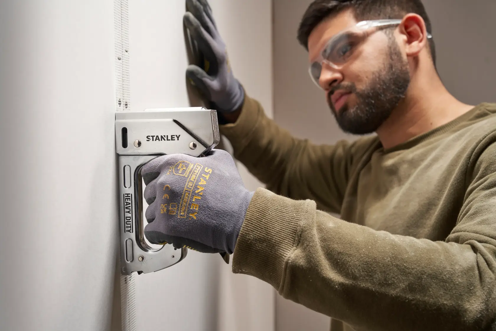Stanley TR110 pistola de grapas de alta resistencia sostenida por mano enguantada en pared, fotografía de primer plano.