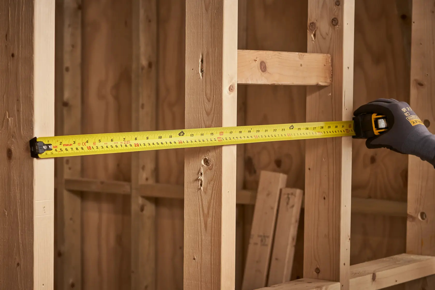 Cinta métrica STANLEY XTHT0-33504 extendida sobre estructura de madera, vista en ángulo, entorno de construcción.