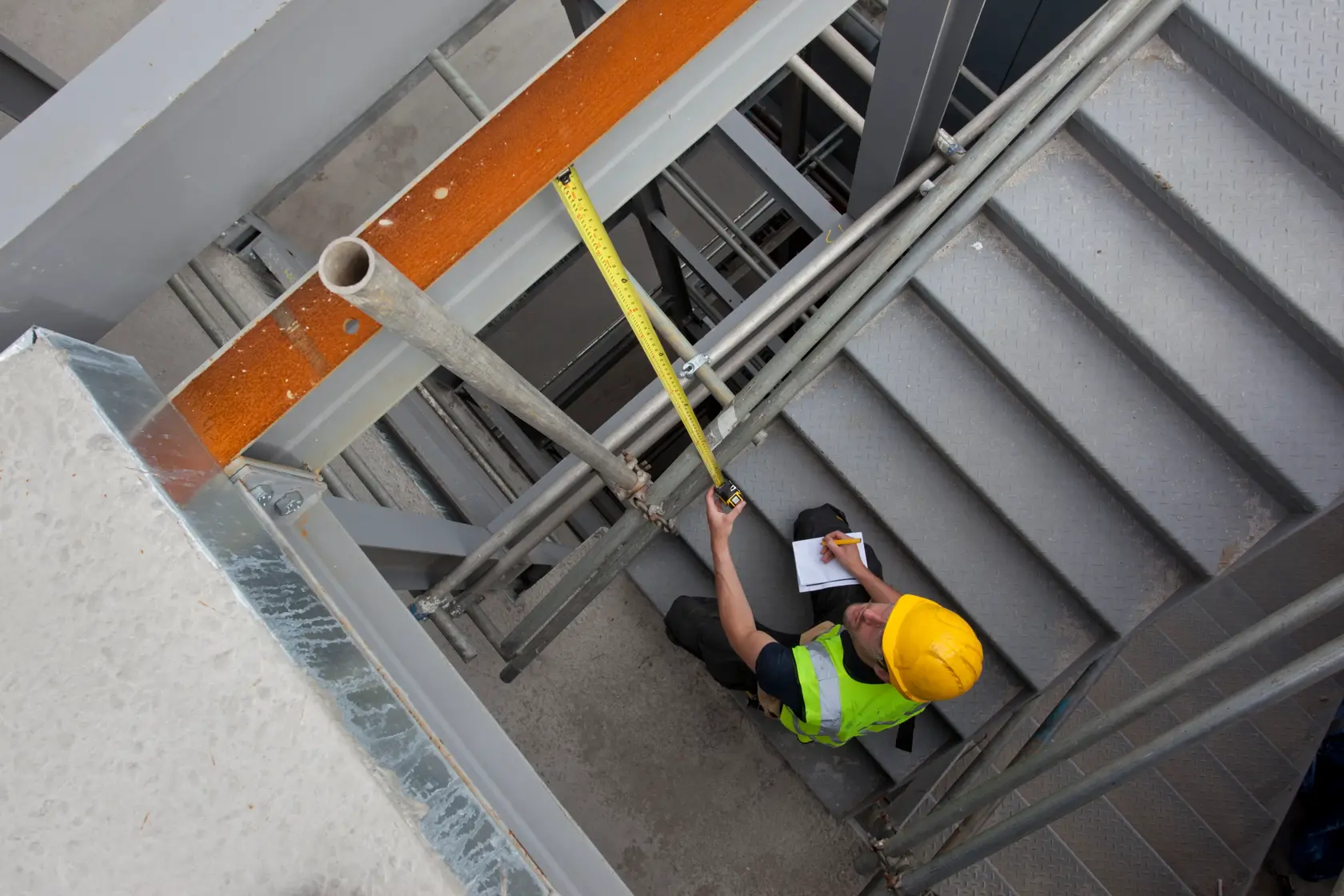 STANLEY XTHT0-33504 cinta métrica usada por trabajador en escaleras en sitio de construcción, vista desde arriba.